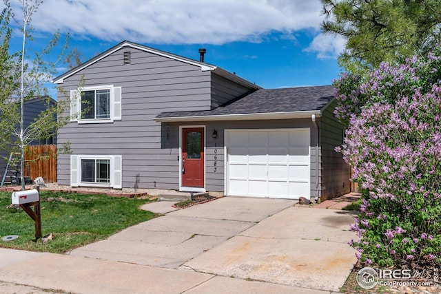 tri-level home with fence, a front yard, roof with shingles, concrete driveway, and an attached garage