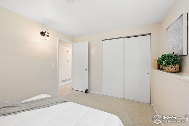 bedroom with a closet, baseboards, light colored carpet, and visible vents