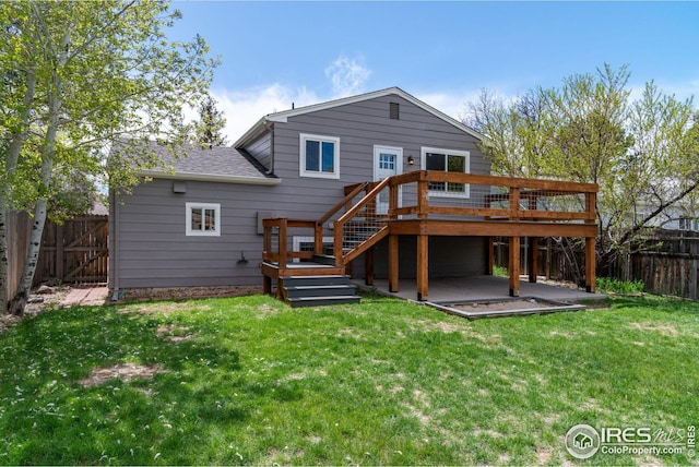 back of house featuring roof with shingles, a deck, a fenced backyard, a patio area, and a lawn