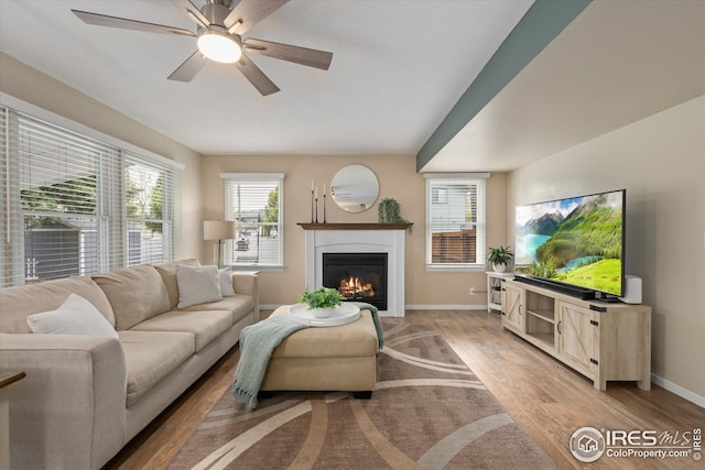 living area with baseboards, a glass covered fireplace, ceiling fan, and light wood-type flooring