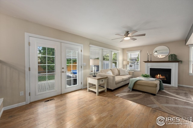 living area featuring ceiling fan, french doors, visible vents, a warm lit fireplace, and hardwood / wood-style floors
