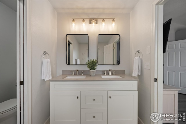 bathroom with toilet, double vanity, baseboards, and a sink