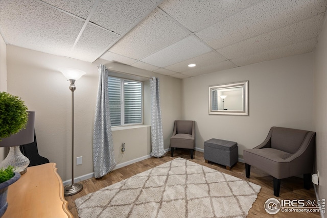 living area with baseboards, wood finished floors, and a paneled ceiling