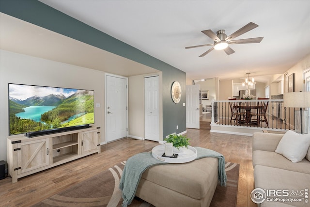 living area featuring baseboards, ceiling fan with notable chandelier, and wood finished floors