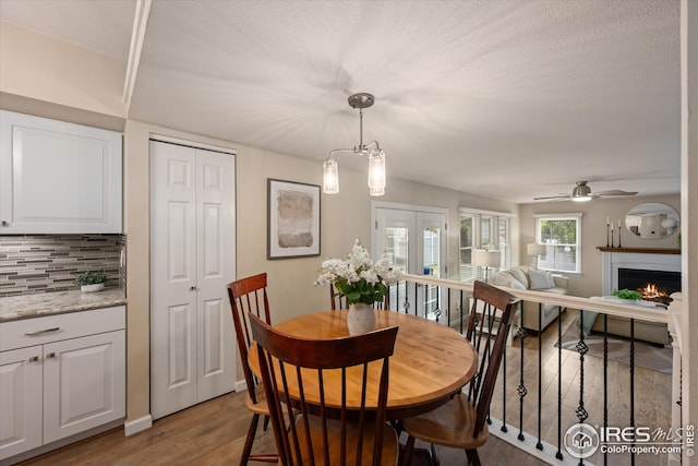 dining room featuring a lit fireplace, a ceiling fan, a textured ceiling, wood finished floors, and baseboards