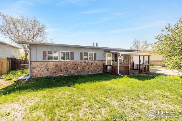 view of front of house with board and batten siding, stone siding, fence, and a front yard