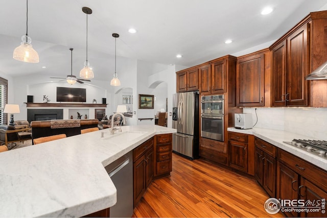kitchen featuring a ceiling fan, wood finished floors, a fireplace, a sink, and stainless steel appliances