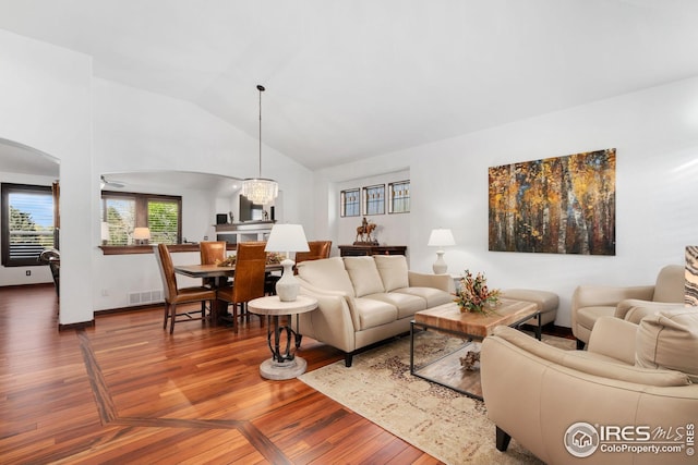 living room featuring arched walkways, visible vents, wood finished floors, and vaulted ceiling
