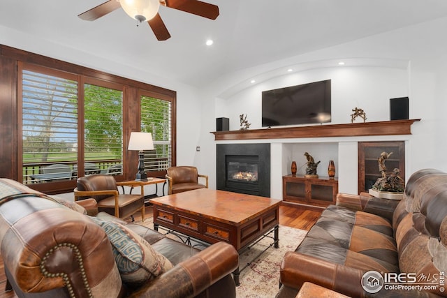 living area with ceiling fan, a glass covered fireplace, recessed lighting, wood finished floors, and lofted ceiling
