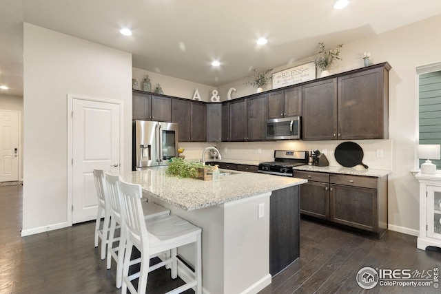 kitchen featuring dark wood finished floors, dark brown cabinets, a sink, light stone counters, and stainless steel appliances