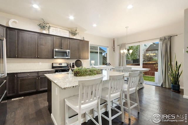 kitchen with dark brown cabinets, appliances with stainless steel finishes, dark wood-style floors, and light stone counters