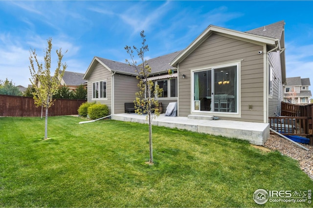 rear view of property featuring a lawn, fence, a shingled roof, and a patio area