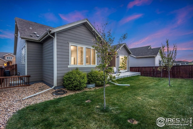 back of house with a yard, fence, and a shingled roof
