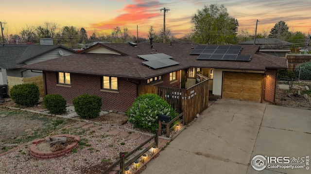 view of front of property with brick siding, a garage, roof with shingles, and solar panels