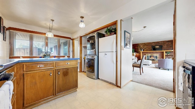 kitchen featuring brown cabinetry, freestanding refrigerator, stacked washer and dryer, and light floors