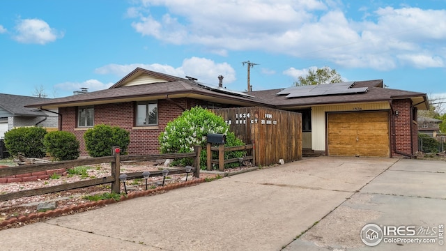 view of front of property with a garage, roof mounted solar panels, driveway, and brick siding