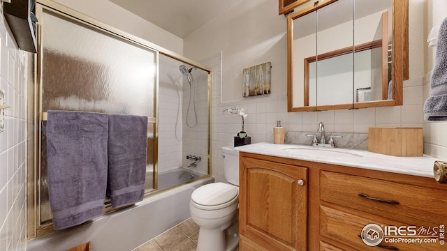 bathroom with tile patterned flooring, vanity, toilet, tile walls, and combined bath / shower with glass door