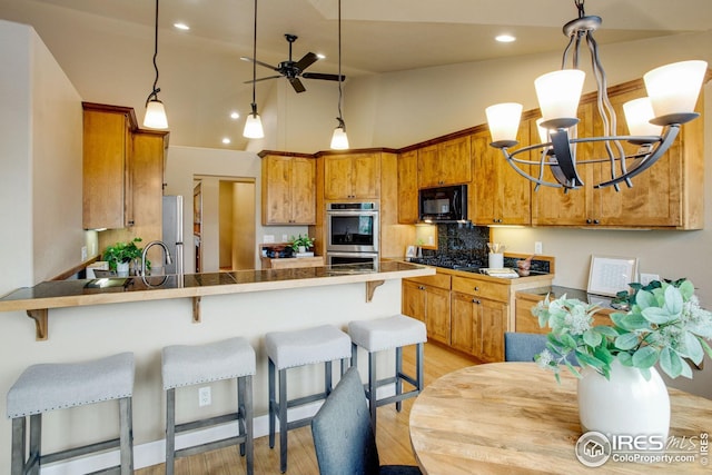 kitchen with a peninsula, ceiling fan with notable chandelier, light wood-style flooring, appliances with stainless steel finishes, and backsplash