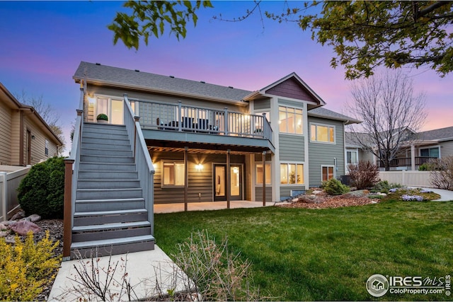 back of house at dusk with a lawn, fence, a deck, and stairway