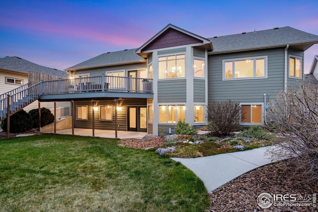 back of property at dusk with a lawn, a deck, stairway, a patio, and a shingled roof