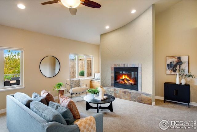 living area with a tiled fireplace, a ceiling fan, baseboards, and carpet floors