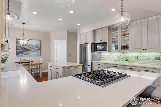 kitchen with appliances with stainless steel finishes, tasteful backsplash, a center island, a notable chandelier, and glass insert cabinets