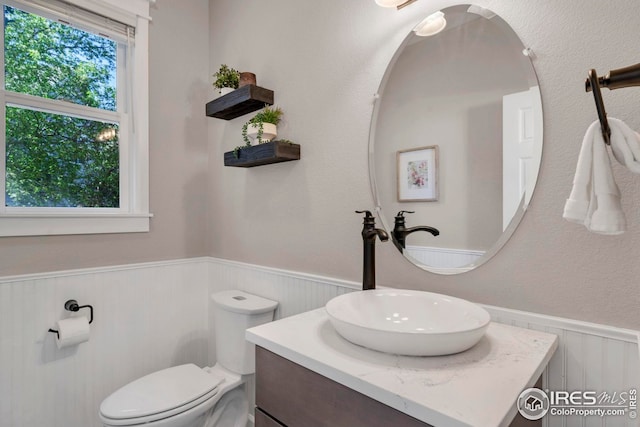 half bath featuring vanity, toilet, wood walls, and a wainscoted wall