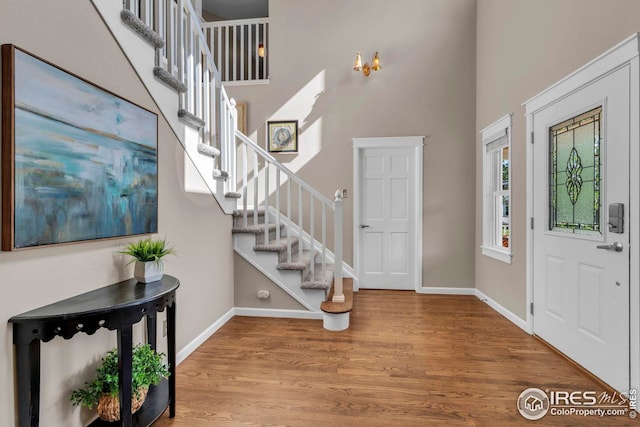 entrance foyer with stairway, baseboards, wood finished floors, and a towering ceiling
