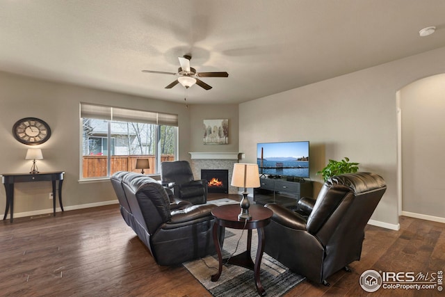 living area featuring dark wood-style flooring, arched walkways, a ceiling fan, baseboards, and a tile fireplace