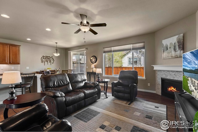 living area with a warm lit fireplace, ceiling fan, recessed lighting, baseboards, and wood finished floors