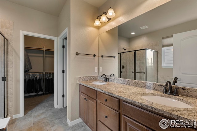 bathroom with double vanity, a walk in closet, a sink, and a stall shower