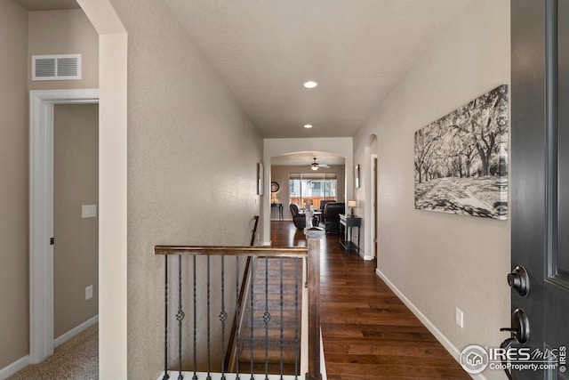hall with visible vents, arched walkways, wood finished floors, an upstairs landing, and recessed lighting