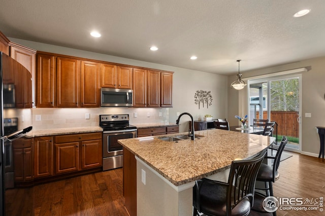 kitchen featuring decorative backsplash, light stone countertops, a sink, dark wood finished floors, and appliances with stainless steel finishes