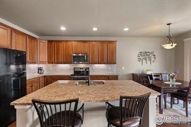 kitchen featuring backsplash, stainless steel appliances, brown cabinets, and an island with sink