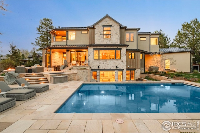 back of property featuring a standing seam roof, metal roof, an outdoor pool, a patio area, and stone siding
