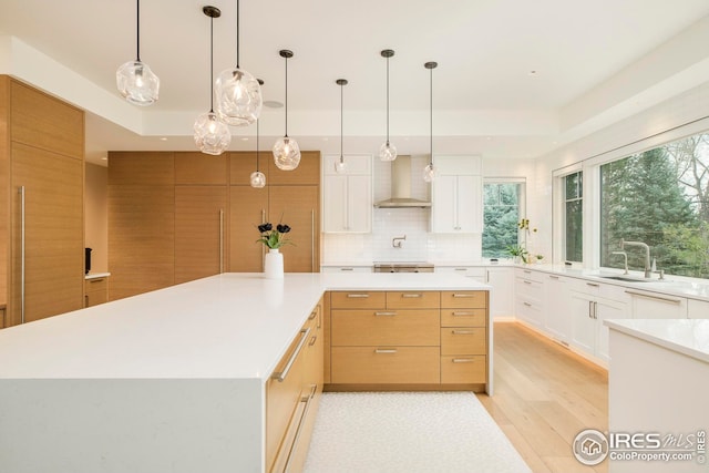 kitchen featuring wall chimney range hood, a sink, light countertops, light wood-style flooring, and a spacious island
