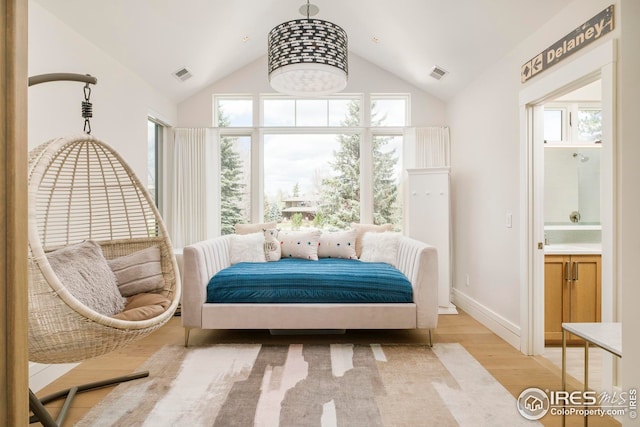 bedroom featuring light wood-style floors, connected bathroom, visible vents, and vaulted ceiling