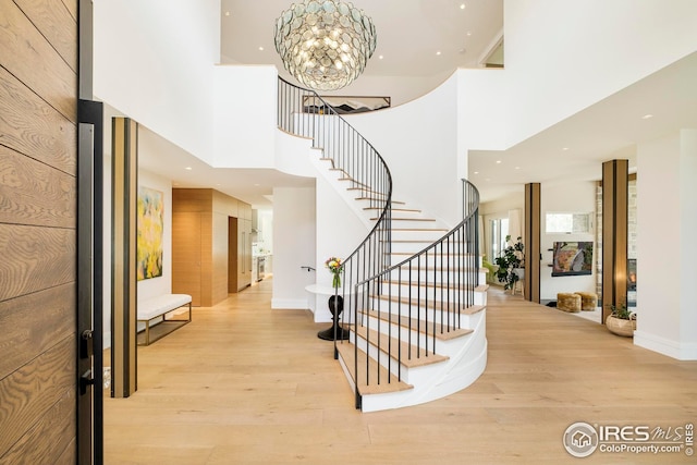 entryway featuring an inviting chandelier, a towering ceiling, light wood-style floors, stairway, and recessed lighting