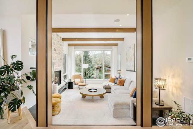 living room with visible vents, wood finished floors, a stone fireplace, and beamed ceiling