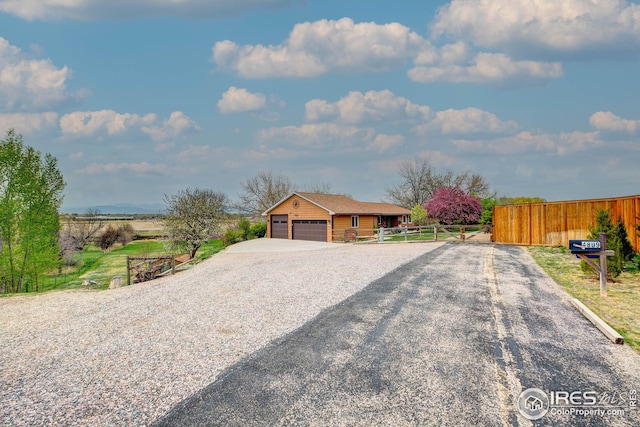 view of front of house featuring fence, an attached garage, and gravel driveway