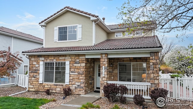 traditional-style home with a porch, fence, a tiled roof, and stone siding