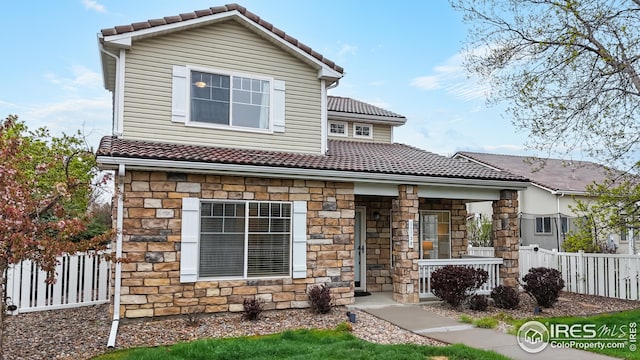 traditional-style house featuring a tiled roof, fence, covered porch, and stone siding