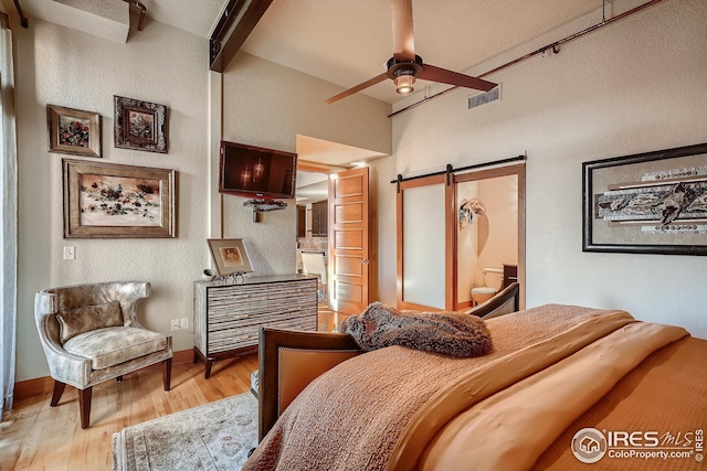 210 W Magnolia St Unit 320, Fort Collins, CO 80521 - bedroom featuring a barn door, baseboards, beamed ceiling, light wood-style floors, and a textured wall