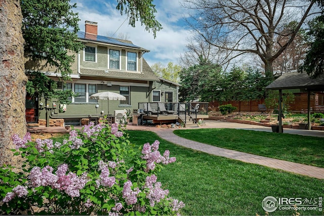 exterior space with a chimney, a deck, fence, roof mounted solar panels, and a yard