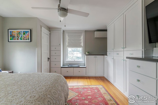 bedroom with a wall mounted air conditioner, light wood-style flooring, and a ceiling fan