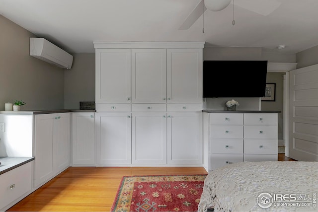 bedroom with ceiling fan, light wood finished floors, and a wall mounted air conditioner