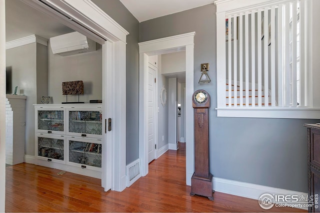 corridor featuring baseboards, visible vents, a wall mounted air conditioner, and wood finished floors