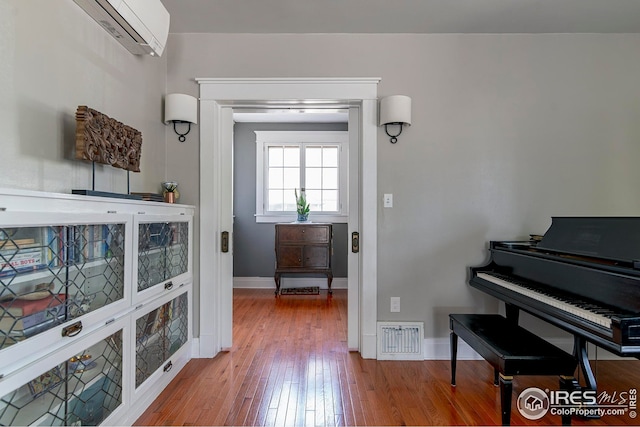 interior space with baseboards, a wall mounted air conditioner, hardwood / wood-style floors, and visible vents