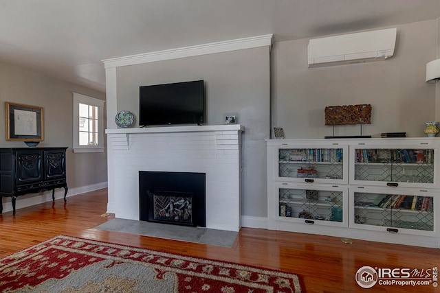 living room featuring wood finished floors, baseboards, a wall mounted AC, and a fireplace