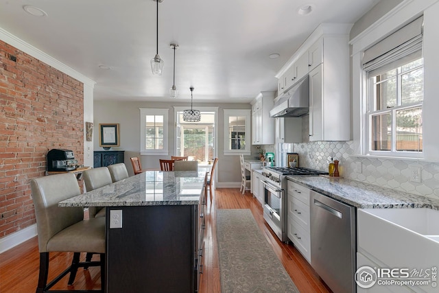 kitchen with light wood-style flooring, stainless steel appliances, baseboards, under cabinet range hood, and a kitchen island
